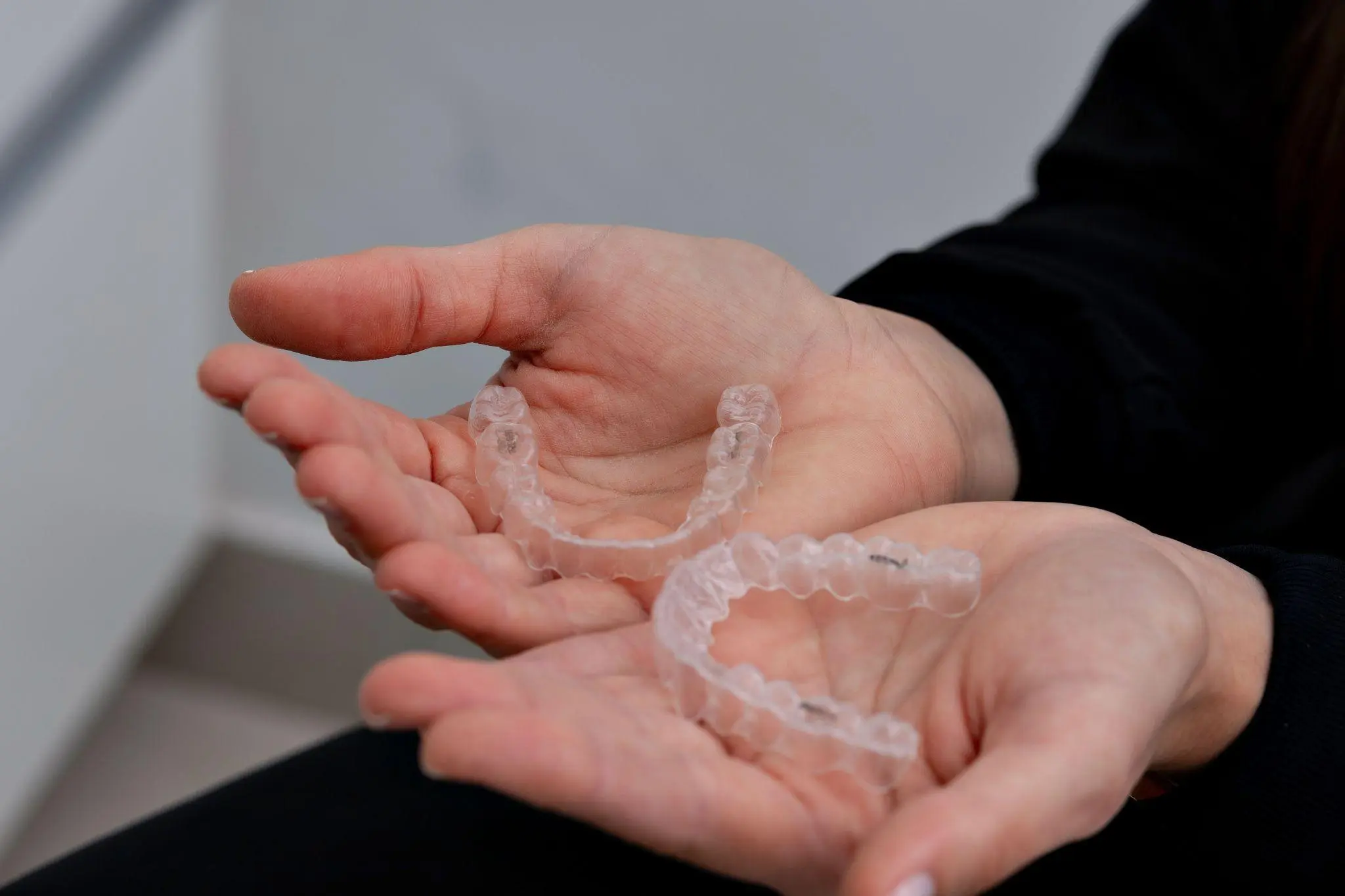 Hands holding a pair of clear Invisalign aligners